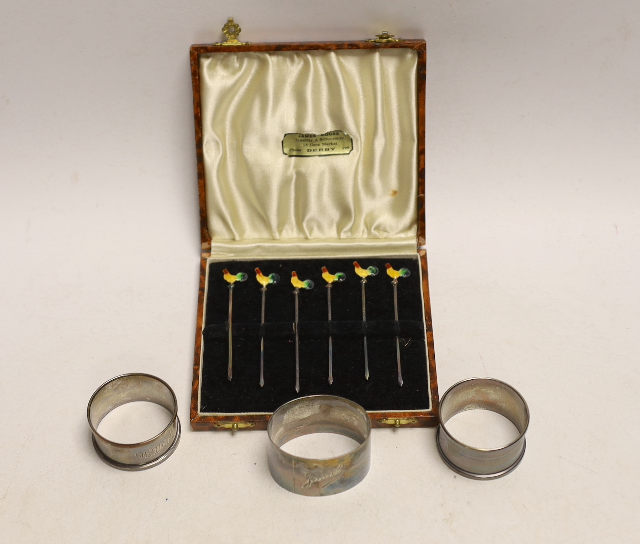 A cased set of six sterling and enamel cocktail sticks, with cockerel terminals and three silver napkin rings.